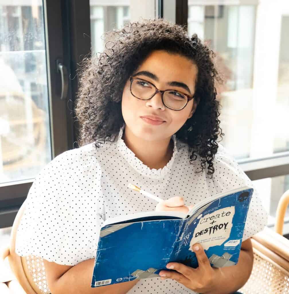 Deep thinking vs Overthinking. Deep thinking example: Woman pausing to think with a workbook about creativity in her hands.